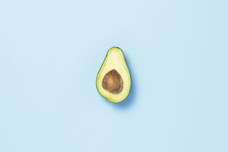Half avocado on a blue background. Healthy eating concept. Minimalism. Flat lay, top view