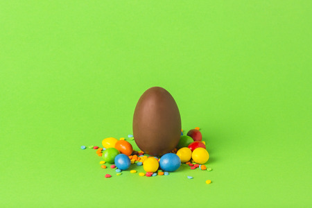 Easter chocolate egg and multi-colored sweets on a green background. Merry Easter celebration conceptの写真素材
