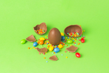 Easter chocolate egg and multi-colored sweets and broken chocolate eggs on a green background. Easter celebration conceptの写真素材
