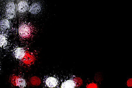 Bokeh night city lights behind wet glass during rain. Can be used as wallpaper or background