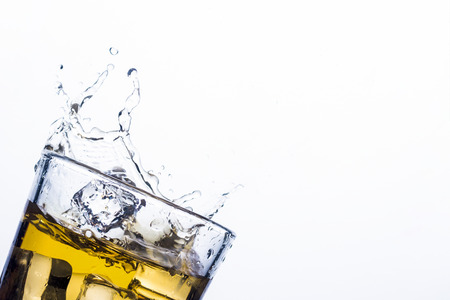 Splash of whiskey from ice cubes on a white background. Concept of alcoholic drinks with ice, whiskey or brandy, apple juice and cooling drinksの写真素材