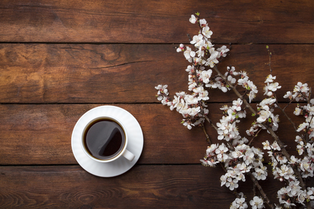 Sakura branches with flowers, White cup with Black Coffee on a dark wooden background. Flat lay, top view.の写真素材