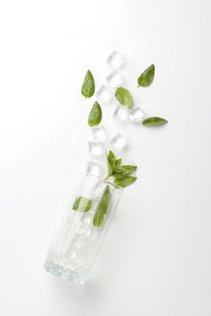 Spilled Glass with refreshing water, mint leaves and ice cubes on a light background.の写真素材