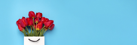 Bouquet of brightly red tulips in a white gift bag on a blue background. Conception of congratulations and a gift. Flat lay, top view.の写真素材