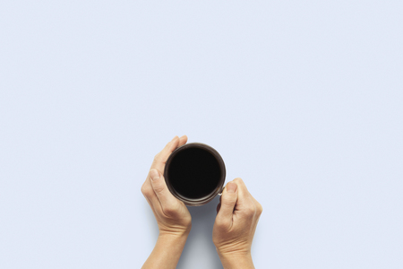Two hands holding a cup with hot coffee on a blue background. Breakfast concept with coffee or tea. Good morning, night, insomnia. Flat lay, top view.の写真素材