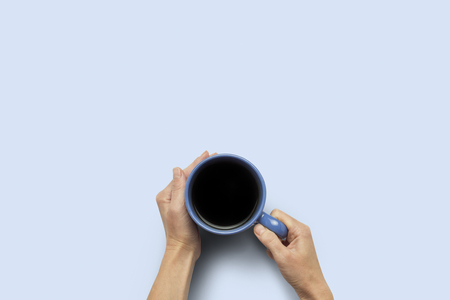 Hand holding a cup with hot coffee on a blue background. Breakfast concept with coffee or tea. Good morning, night, insomnia. Flat lay, top view.の写真素材