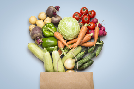 Paper shopping bag and fresh organic vegetables on a blue background. Concept of buying farm vegetables, taking care of health, vegetarianism. Country style, Farm Fair. Flat lay, top view.の写真素材
