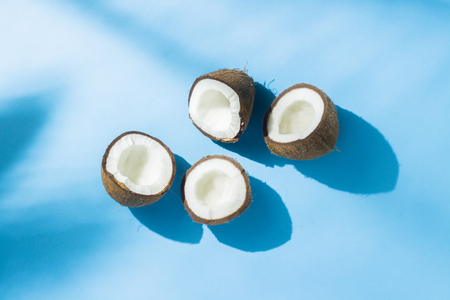 Broken coconut on a blue background under natural light with shadows. Hard light. Concept of diet, healthy eating, rest in the tropics, vacation and travel, vitamins. Flat lay, top viewの写真素材