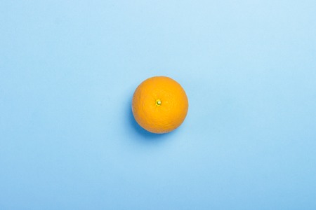 Orange on a blue background. Minimalism. Concept of tropics, healthy eating, vitamins. Flat lay, top...
