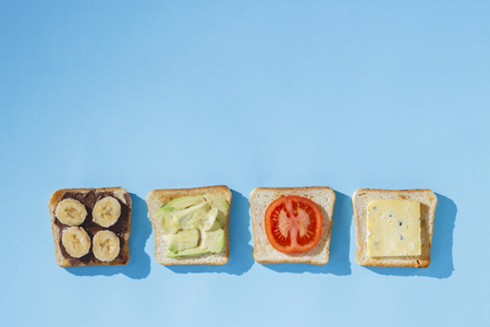 Sandwiches with cheese, tomato, banana and avocado on a blue background. Concept of healthy eating, breakfast at the hotel, diet. Natural lighting, hard light. Flat lay, top viewの写真素材