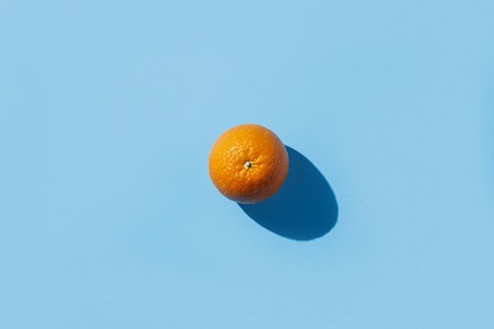 One orange on a blue background. Hard light. Tropics concept, healthy food, breakfast, diet, vacation. Flat lay, top view.の写真素材