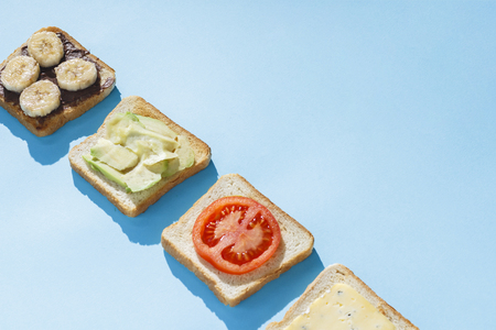 Sandwiches with cheese, tomato, banana and avocado on a blue background. Concept of healthy eating, breakfast at the hotel, diet. Natural lighting, hard light. Flat lay, top viewの写真素材