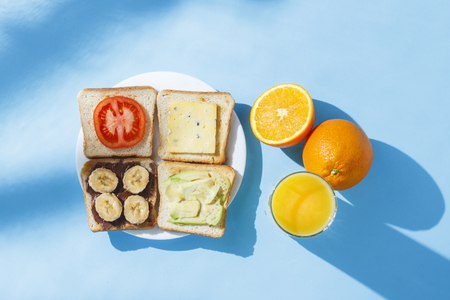 Sandwiches on a white plate, a glass with orange juice in oranges, blue background. Concept of healthy eating, breakfast at the hotel, diet. Natural lighting, hard light. Flat lay, top viewの写真素材