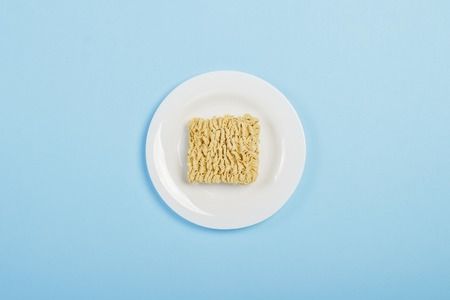 Asian instant noodles on a white plate against a blue background. The concept of convenience foods,...