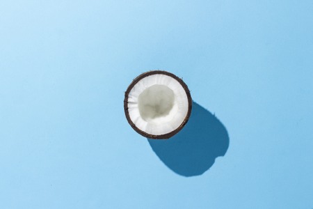 Half coconut on a blue background. Minimalism. Concept of tropics, healthy eating. Flat lay, top viewの写真素材