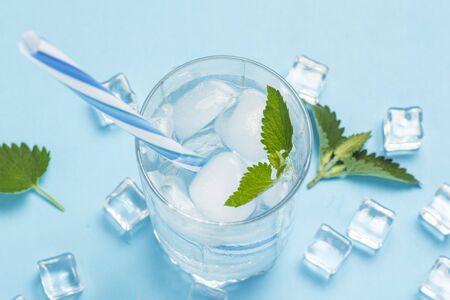 Glass of cold and refreshing water with ice and mint on a blue background. Ice Cube. Concept of hot summer, alcohol, cooling drink, thirst quenching, bar. Flat lay, top view.の写真素材
