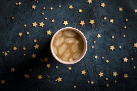 Coffee with ice and milk in a glass on a dark blue stone background with stars. Concept cooling drink, thirst, summer, starry sky, nightlife, insomnia. Flat lay, top view.の写真素材