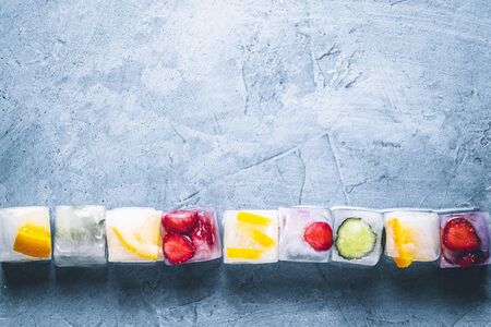 Ice cubes with fruit on a stone blue background. Line. Mint, strawberry, cherry, lemon, orange. Flatlay, top view.の写真素材