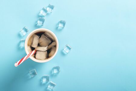 Refreshing iced coffee in a glass and ice cubes on a blue background. Concept summer, cola with ice, refreshing cocktail, thirst. Flat lay, top view.の写真素材