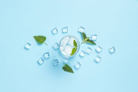 Glass of cold and refreshing water with ice and mint on a blue background. Ice Cube. Concept of hot...
