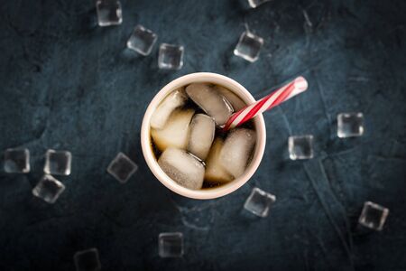 Iced coffee in a glass on a dark blue stone background with ice cubes. Concept cooling drink, thirst, summer, cola with ice, nightlife, club. Flat lay, top view.の写真素材