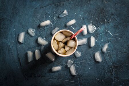 Iced coffee in a glass on a dark blue stone background with ice cubes. Concept cooling drink, thirst, summer, cola with ice, nightlife, club. Flat lay, top view.の写真素材