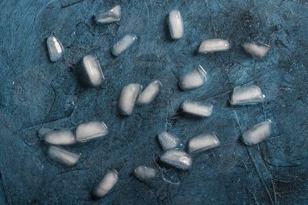 Ice cubes on a dark blue stone background. Flat lay, top view.