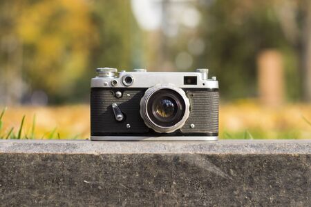 Camera lies on the curb in an autumn park with yellow leaves.