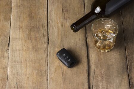 A glass with spilled alcoholic beverage and car keys on a wooden background. Drunk driving concept,...