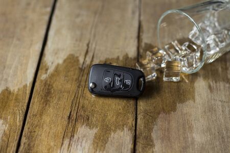 A glass with spilled alcoholic beverage and car keys on a wooden background. Drunk driving concept, stop drinking and drivingの写真素材