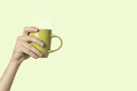 Female hand holding a green cup with hot coffee or tea on a light green background. Breakfast concept with hot coffee or tea.の写真素材