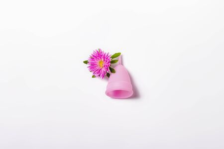 Pink menstrual cup and flower on a white background. Concept of menstruation, the choice between feminine hygiene products. Flat lay, top.の写真素材