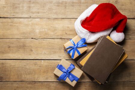 Santa Claus hat, gift, books on wooden background. The concept of Christmas, winter holidays, new year. Flat lay, top view.の写真素材