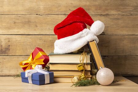 Pile of books, Santa Claus hat, Christmas-tree decorations and Gifts on a wooden background. Holiday concept, christmas, christmas eve.の写真素材