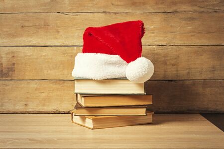 Stack of books, Santa's hat on a wooden background. Holiday concept, christmas, christmas eve.の写真素材