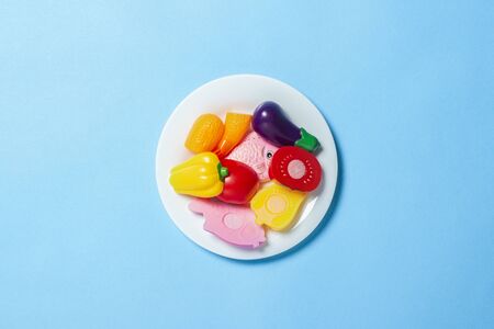 White plate with children's toys in the form of food on a blue background. Concept Artificial food, proper nutrition, diet, convenience foods. Flat lay, top view.の写真素材