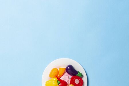 White plate with children's toys in the form of food on a blue background. Concept Artificial food,...