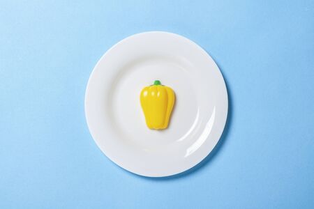 White plate with plastic peppers paprika toys in the form of food on a blue background. Concept...