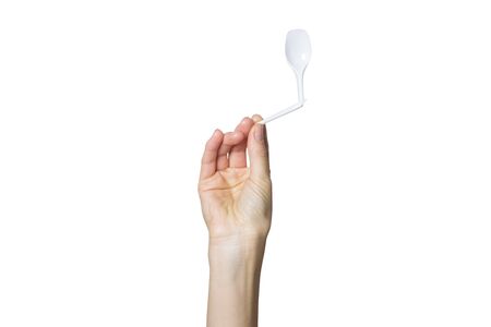 Female hand holds a broken plastic spoon on a white isolated background. The concept of separate trash, stop plastic, recycling.の写真素材