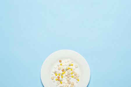 A lot of pills on a white plate on a blue background. Insomnia, a choice of drugs, vitamins, weight loss through farm drugs. Flat lay, top view.の写真素材
