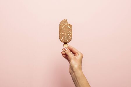 Female hand holds a bitten ice cream on a stick on a pink background. Concept of hot summer, stress. Flat lay, top view.の写真素材