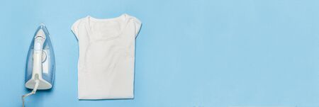 Iron for ironing things and a white T-shirt on a blue background. Laundry concept, atelier, housework. banner. Flat lay, top view.の写真素材