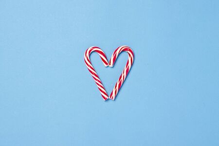 Candy caramel cane in the form of a heart on a blue background. Concept Christmas, New Year, minimalism. Flat lay, top view.の写真素材