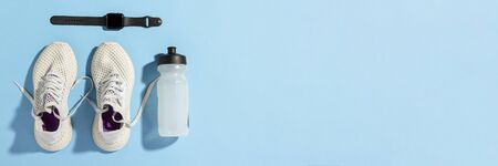 Fitness tracker, White sneakers and a bottle of water under morning sunlight on a blue...