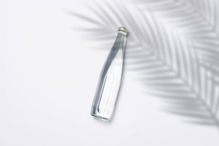 Bottle of pure crystal water on a white background under palm leaves and sunlight. Banner. Concept of thirst, heat, summer, tropic. Flat lay, top view.の写真素材