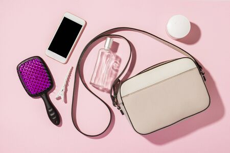 Women's QUILTED CROSSBODY BAG with a long handle and accessories, phone, comb, perfume, cream on a pink background. Banner. Concept of fashion and beauty, modern, stylish. Flat lay, top view.の写真素材
