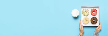 Female hands hold a box with donuts, a cup of coffee on a blue background. Concept confectionery...