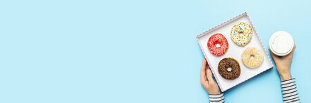 Female hands hold a box with donuts, a cup of coffee on a blue background. Concept confectionery...