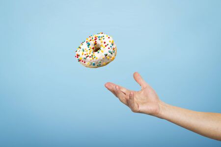Hand catch a donut with icing. Blue cardboard background. Concept of baking, handmade. Flat lay, top...