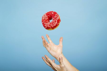 Hands catch a donut with icing. Blue cardboard background. Concept of baking, handmade. Flat lay, top view.の写真素材